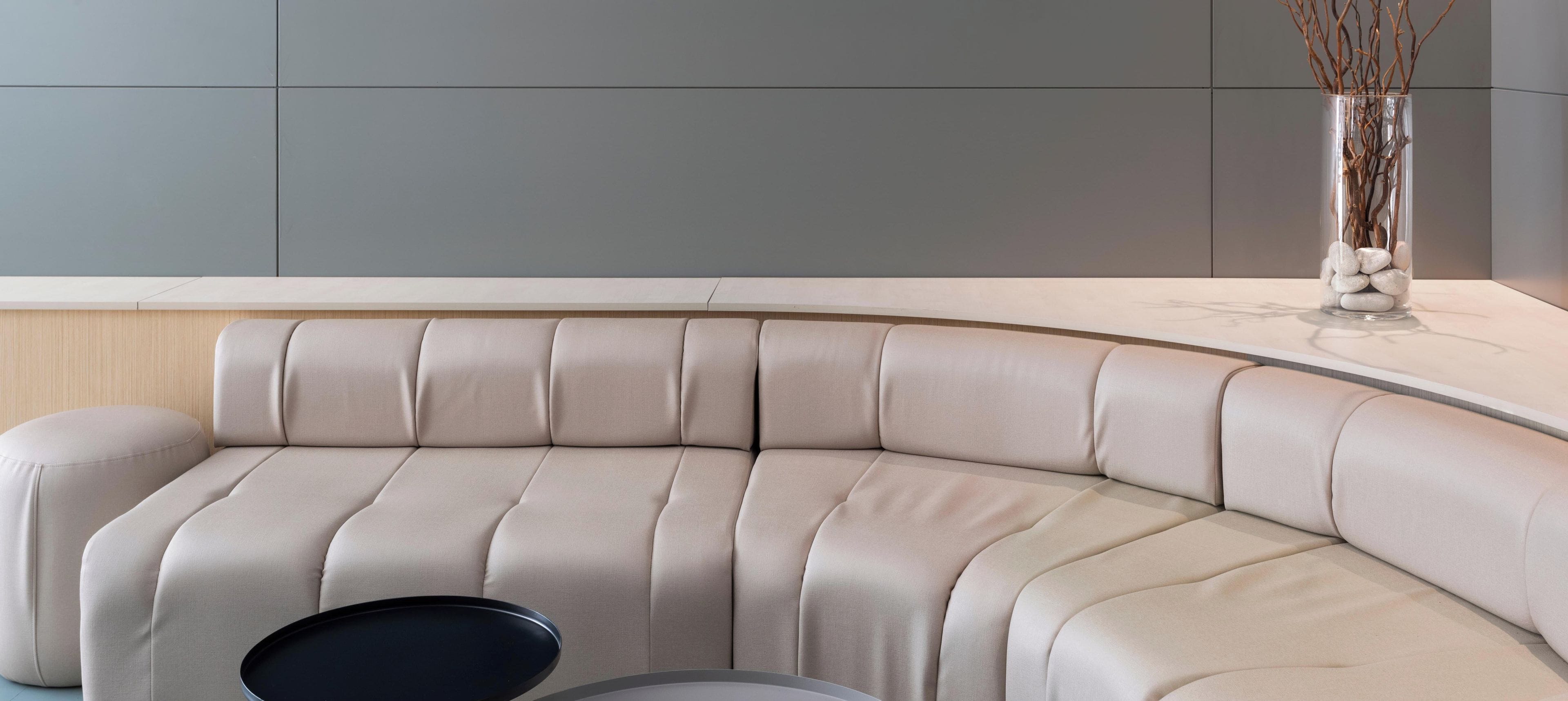 Un sofá moderno de líneas curvas con respaldo y reposabrazos acolchados, ubicado en una habitación contemporánea con una paleta de colores neutros.