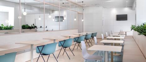 A modern dining area with long tables and chairs, a large mirror, and a flat-screen TV on the wall.