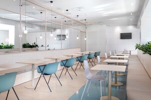 A modern dining area with long tables and chairs, a large mirror, and a flat-screen TV on the wall.