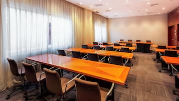 Un salón de conferencias con varias mesas y sillas, ventanas amplias con cortinas y piso alfombrado.