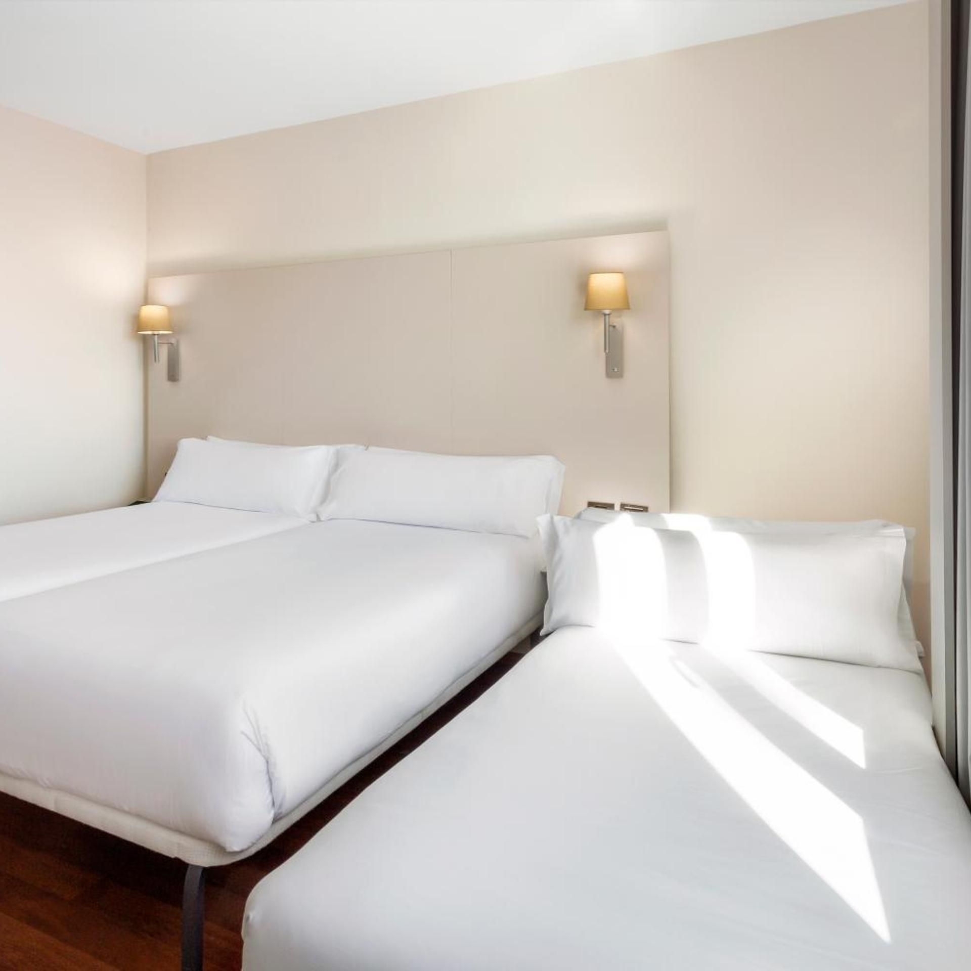 Habitación de hotel con dos camas, cabeceros y lámparas fijadas a la pared.