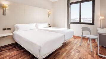 A hotel room with two beds, a desk, a chair, and a large window.