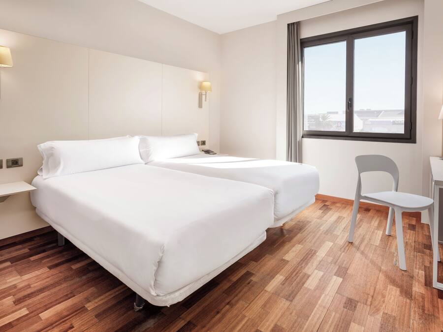 A hotel room with two beds, a desk, a chair, and a large window.