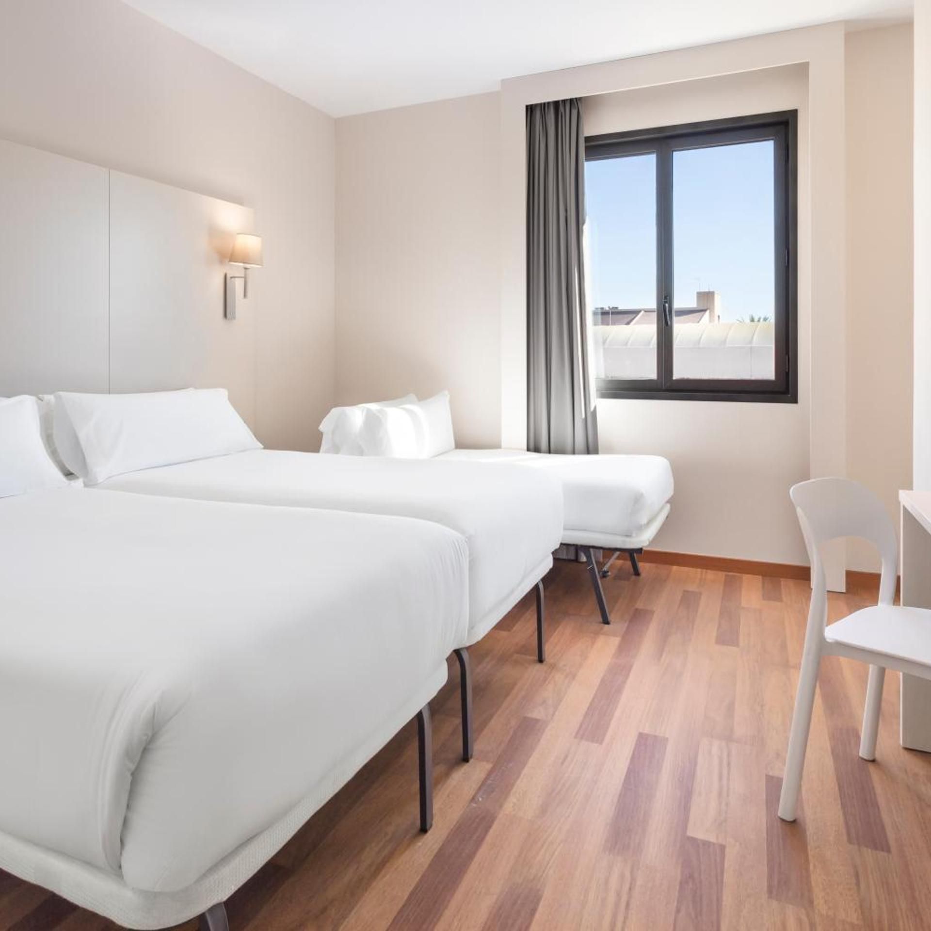 A hotel room with two beds, a desk, and a window with a view.