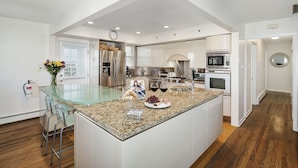 A modern kitchen with a central island, stainless steel appliances, and a glass-top table.