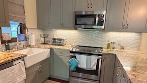 A kitchen with grey cabinets, a stainless steel microwave, an oven, a sink, and a window with a view. - Riverfront, Hot tub, shared pool, minutes to slopes with large covered deck! (Banner Elk)