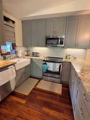 A kitchen with grey cabinets, a stainless steel microwave, an oven, a sink, and a window with a view.
