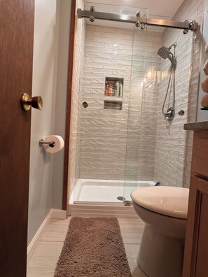 A bathroom with a glass-enclosed shower, a toilet, a towel rack, and a small shelf with toiletries. - Riverfront, Hot tub, shared pool, minutes to slopes with large covered deck! (Banner Elk)