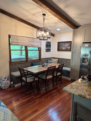 A kitchen with a wooden table, chairs, a built-in bench, a hanging light fixture, and a refrigerator.
