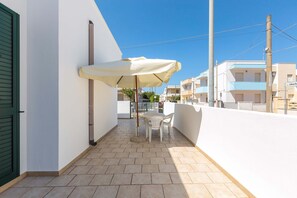 Een balkon met een witte tafel en stoelen, een beige parasol en uitzicht op omliggende gebouwen.