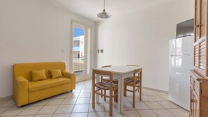 Una cocina compacta con una mesa de comedor, sillas, un sofá amarillo y un refrigerador.