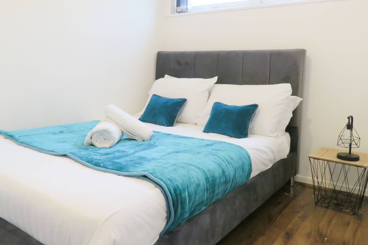 Ein ordentlich bezogenes Bett mit grauem Kopfteil, einer blauen Decke und zwei Kissen.