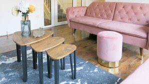 Ein Wohnzimmer mit einem rosafarbenen Sofa, einem Holztisch und einem rosafarbenen Hocker.