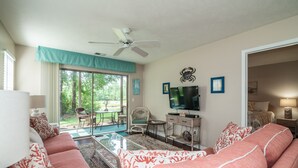 A living room with a sofa, television, and a view of the outdoors. - TB 12A First Floor 3BR/3BA with great view of golf course w/no stairs (PAWLEYS ISLAND)