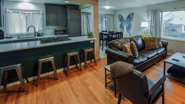 Een moderne keuken met een centraal eiland, barkrukken, een eethoek met een bank en stoelen, en een wanddecoratie van een vlinder.