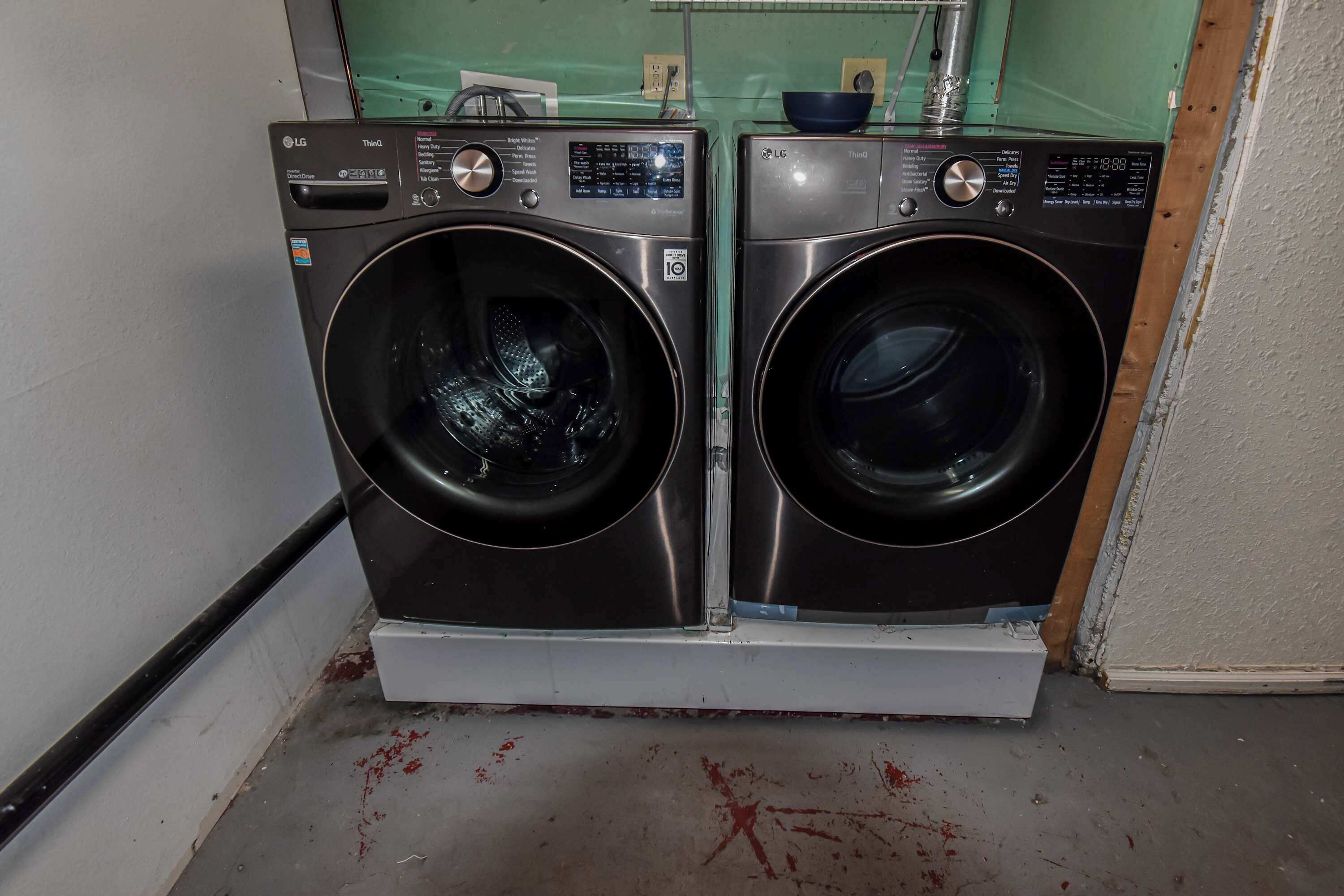 Two front-loading LG washing machines in a laundry room with a green wall and a white door.