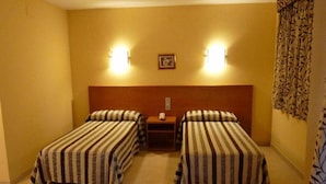 Ein Hotelzimmer mit zwei Einzelbetten, einem Holzkopfteil, einem kleinen Nachttisch und zwei Wandleuchten.