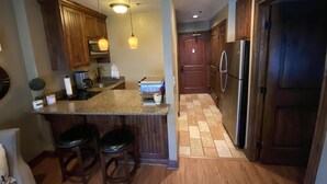 Une cuisine dotée de plans de travail en granit, de meubles en bois, d’un réfrigérateur en acier inoxydable et de deux tabourets de bar.