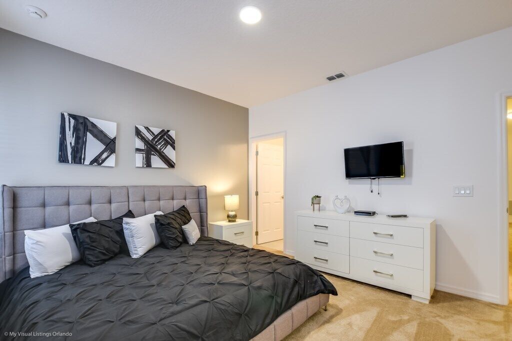 A bedroom with a bed, a TV, a dresser, and abstract wall art.