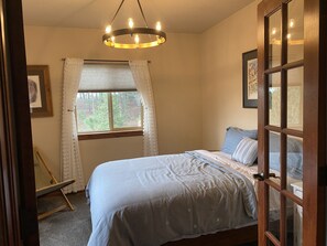 A bedroom with a bed, a window with curtains, a chandelier, and a door with glass panels. - Serene Retreat Nestled in the pines- private & relaxing; Microweddings; Reunions (Colorado Springs)