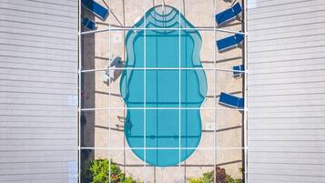 A swimming pool with a grid structure, surrounded by lounge chairs, and bordered by a building facade.