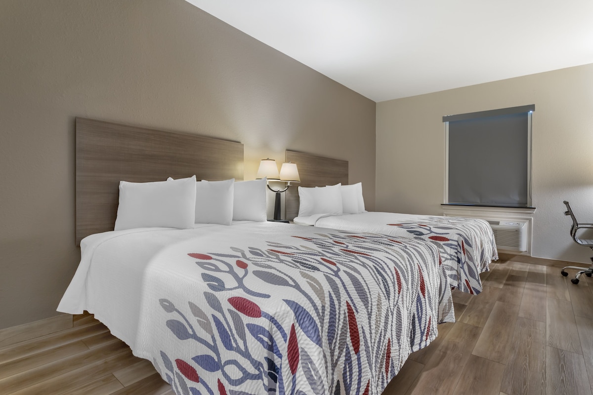 A hotel room with a large bed, a nightstand with a lamp, a window, and a view of the outside.
