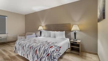 Quarto de hotel com uma cama grande, duas luminárias de cabeceira, uma cadeira, uma escrivaninha e uma janela.