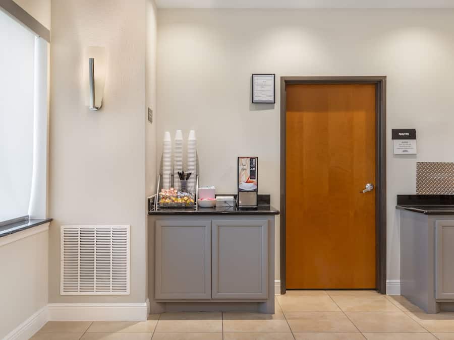 Uma área de recepção com porta de madeira, balcão com alimentos e uma ventilação na parede.
