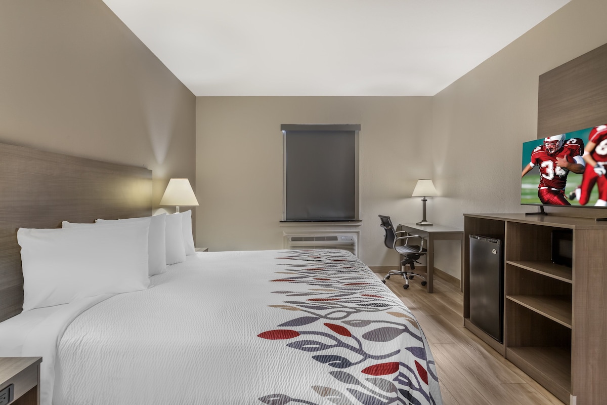 A hotel room with a large bed, a desk, a television, and a minibar.