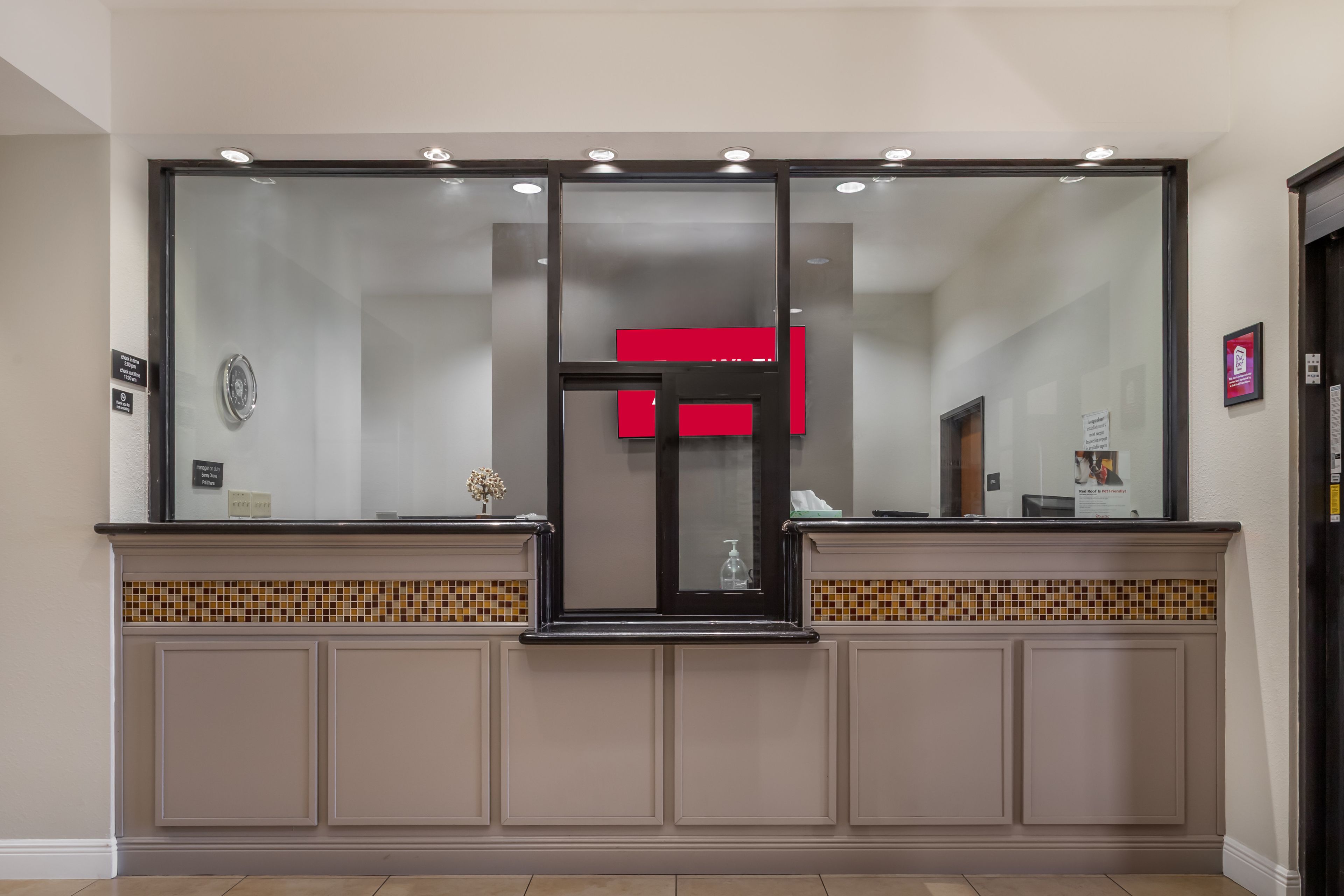 Uma área de recepção com divisória de vidro, uma placa vermelha e painel de azulejos.