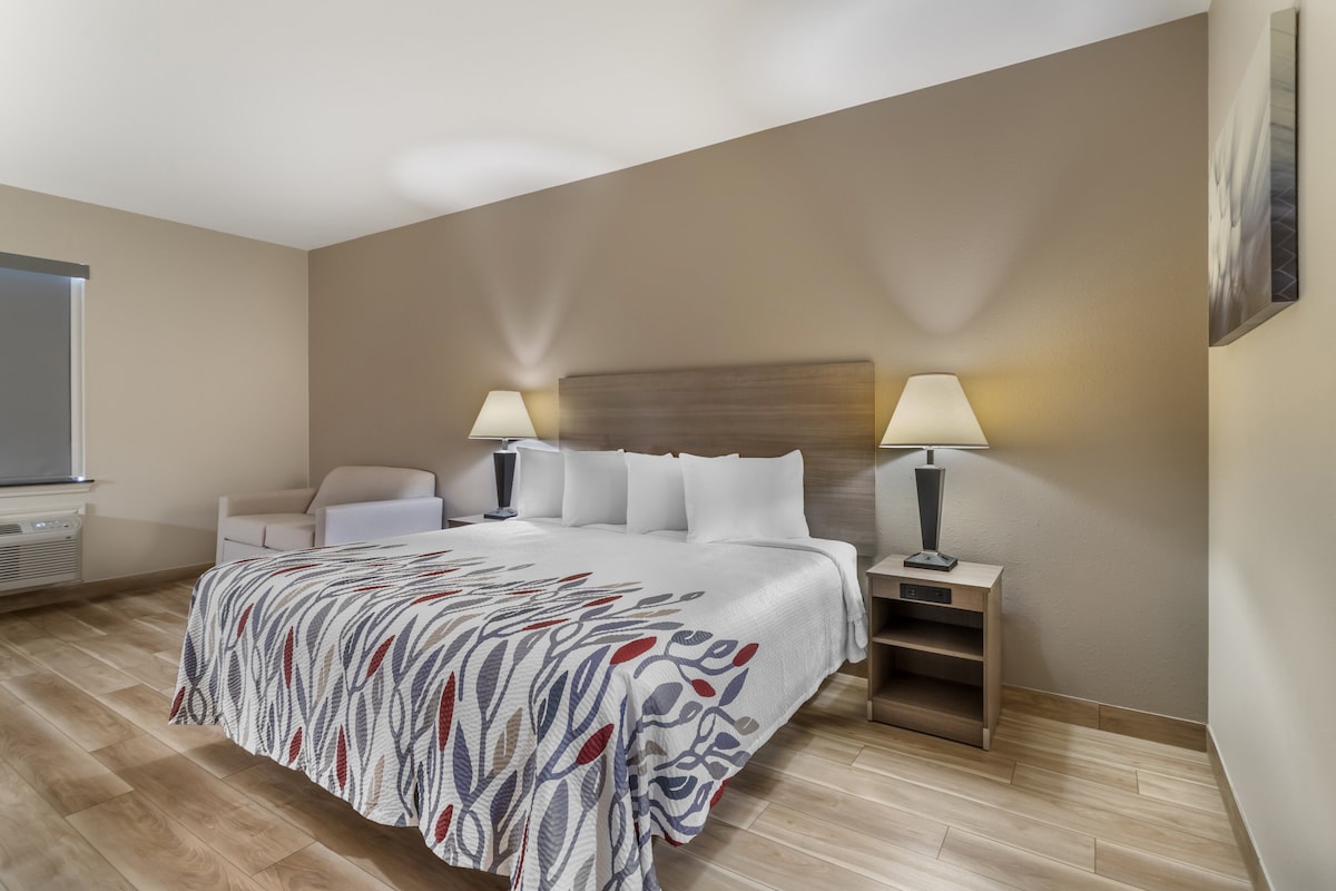 A hotel room with a large bed, two bedside tables with lamps, a chair, and a window.