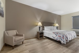 Una habitación de hotel con cama, mesitas de noche, una silla y una ventana.