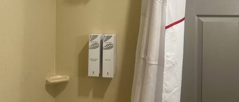 A bathroom with a shower, a toilet, and two boxes of True Red shampoo and bath gel.