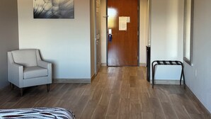 A hotel hallway with a wooden floor, a grey armchair, a door with a notice, and a mirror on the wall. - Red Roof Inn La Porte (La Porte)
