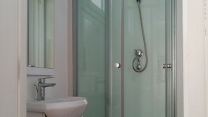 Ein modernes Badezimmer mit einer Duschkabine aus Glas, einem weißen Waschbecken und einem Spiegel.