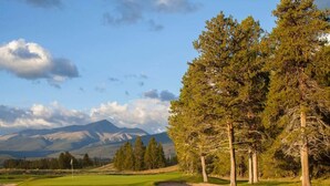 Ein Golfplatz mit Fahne, Bäumen und Bergen im Hintergrund.