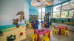 Ein Kinderraum mit bunten Wandgemälden, Tischen, Stühlen und Regalen.