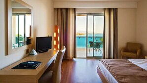 Ein Hotelzimmer mit Bett, Schreibtisch mit Computer, Stuhl und Meerblick durch große Fenster.