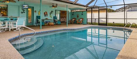 Una piscina exterior techada con ventilador de techo, sillas y un patio con vistas al jardín trasero.