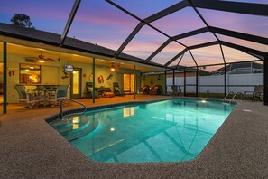 An indoor swimming pool with a covered patio area, seating, and a view of the sunset. - Outdoor Kitchen, Pet-friendly, Pool & Hot tub - Villa Tropical Paradise - Roelens Vacations (Cape Coral)