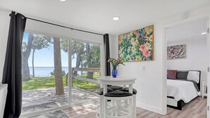 Una habitación con cama, una mesita con sillas, un cuadro y vista al exterior.