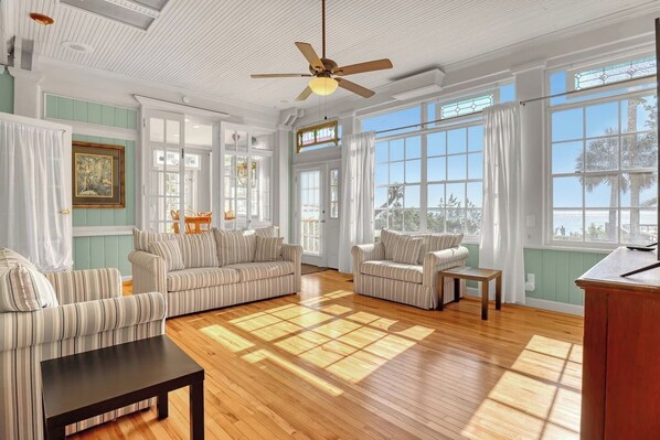 A spacious living room with a wooden floor, two striped sofas, a small table, and a ceiling fan.