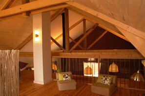 Een zolderkamer met houten balken, een hoge plafond en twee banken met kussens.