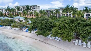 A beachfront hotel with multiple buildings, palm trees, and a sandy beach with lounge chairs.