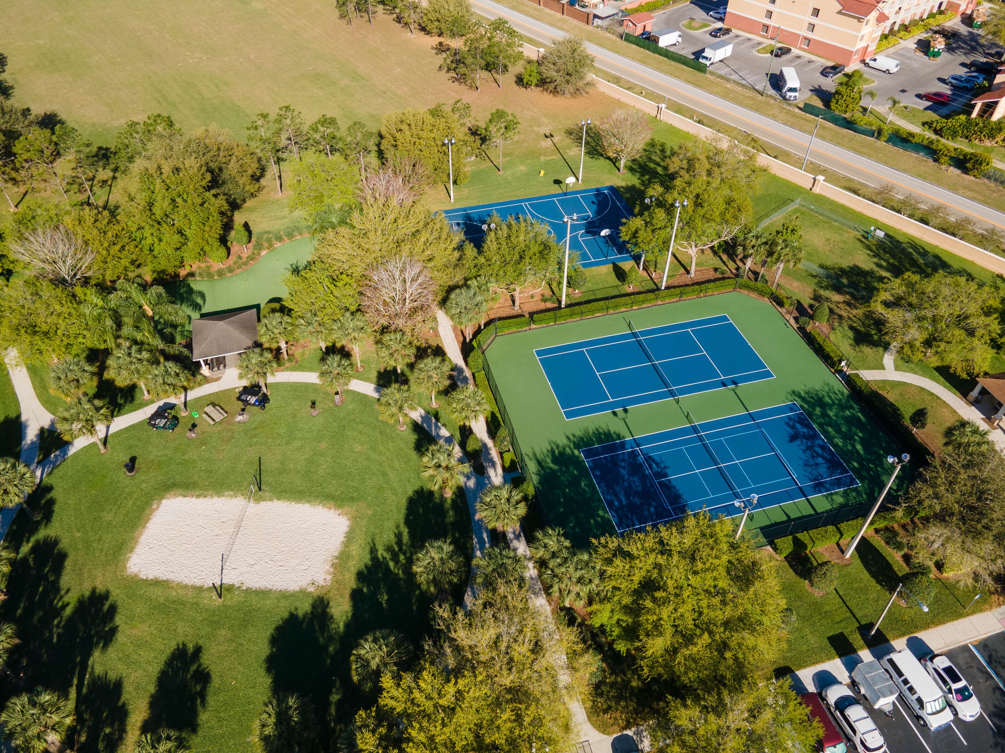 Vue aérienne d’un complexe de courts de tennis comprenant plusieurs terrains, entouré d’arbres et d’un parking.
