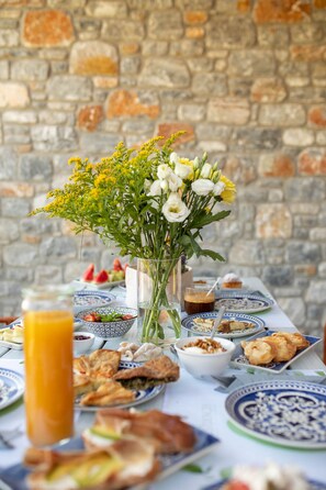 Una mesa servida con diversos platos, un vaso de jugo de naranja y un florero contra una pared de piedra.