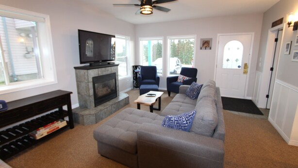 A living room with a fireplace, a sofa, a television, and a ceiling fan. - Cozy ground level suite with private hot tub - close to the Attridge Chair (Silver Star Mountain)
