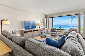 A modern living room with a large sofa, a television, and a view of the ocean. - Special Summer Rate 8/8-9/12 $450 -Oceanfront Corner 3bd/2ba - SK 237 (Lahaina)