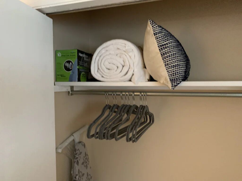 Un placard avec une étagère contenant une serviette enroulée, un oreiller et une boîte.