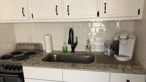 Een keuken met witte kasten, een roestvrijstalen spoelbak, een fornuis en een koffiezetapparaat.